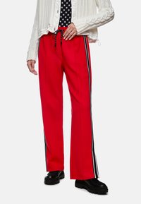 Red wide-leg pants with black and white side stripes. Smooth fabric, elastic waistband with drawstring. Paired with a knitted white sweater.