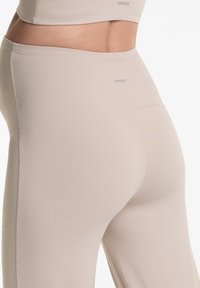 Beige legíny na cvičenie s hladkým, elastickým materiálom. Majú stredne vysoký pás a minimálne švy pre elegantný siluet.