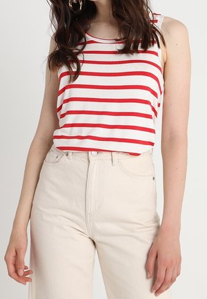 Top sin mangas a rayas rojas y blancas con un corte relajado, combinado con pantalones de mezclilla crema de tiro alto. Tejido de algodón suave y diseño minimalista.