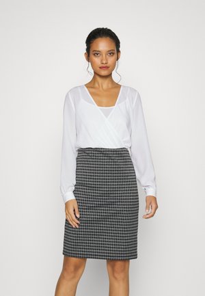 Blusa branca de manga longa com decote V e design em camadas. Saia lápis em preto e branco com padrão xadrez, até ao joelho, de forma ajustada. Textura suave.