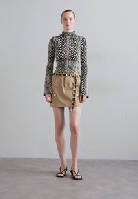 Maglietta a maniche lunghe a righe bianche e nere abbinata a una mini gonna beige con cerniera laterale e accessori circolari in oro. Tacchi neri.