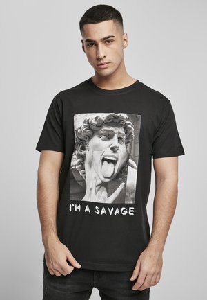 Sort bomulds t-shirt med et stort monokromt grafisk tryk af et skulpturansigt med en stikkende tunge og teksten "JEG ER EN VILDKAT" nedenfor.