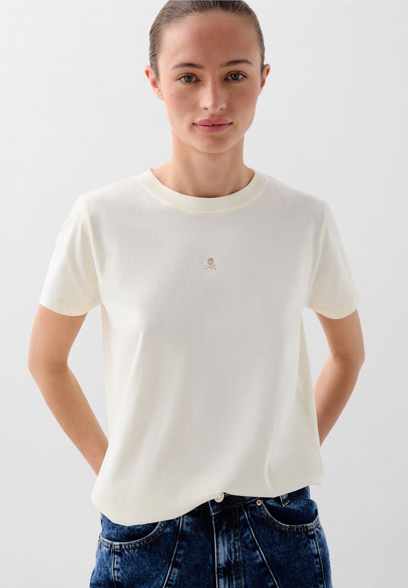 Cremefarbenes Baumwoll-T-Shirt mit kurzen Ärmeln und rundem Ausschnitt, ausgestattet mit einem kleinen gestickten Logo auf der Brust. Glatte Textur, lässige Passform.
