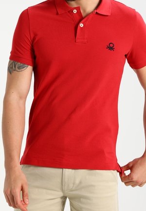Camiseta polo roja de algodón con cuello clásico, mangas cortas y un logo negro en el pecho. Cuenta con cierre de dos botones y ajuste slim.
