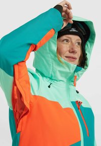 Felle teal en oranje skijas met een capuchon, voorzien van een ritszak, mesh voering en verstelbare trekkoorden. Getextureerde stof.