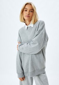 Grauer oversized Sweatshirt mit ribbeligem Saum und Bündchen, ausgestattet mit einem Rundhalsausschnitt. Kombiniert mit passenden Jogginghosen aus demselben Material.