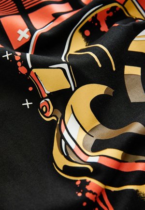 Tessuto nero con una stampa grafica contenente elementi stilizzati in oro e rosso, che includono forme astratte e pattern di spruzzi.