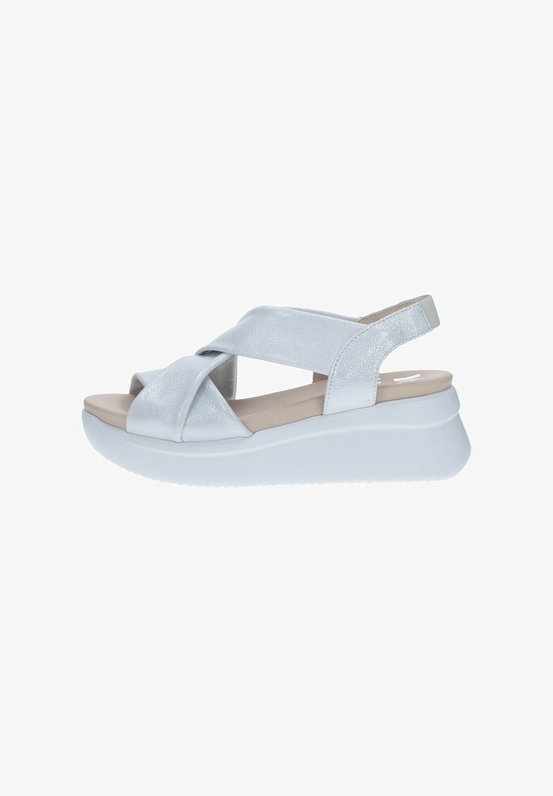 Sandalias de cuña plateadas y blancas con un diseño de tiras cruzadas. Presentan una textura suave y brillante y una plantilla acolchada. Cierre trasero con suela de goma.