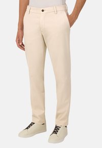 Šviesiai rusvos, lengvos keln�ės su tiesiu kirpimu, turinčios priekinį mygtuko užsegimą ir šonines kišenes, derinamos su kreminėmis sportinėmis bateliais.