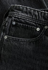 Zwarte denim jeans in close-up, met een voorzak, zilveren klinknagels en een gestructureerde stof met subtiele vervagingdetails.