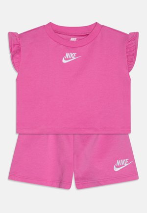 Ružový bavlnený dvojdielny set obsahujúci top s krátkymi rukávmi s volánikmi a zodpovedajúce šortky, ktoré majú obidve biele logo Nike.