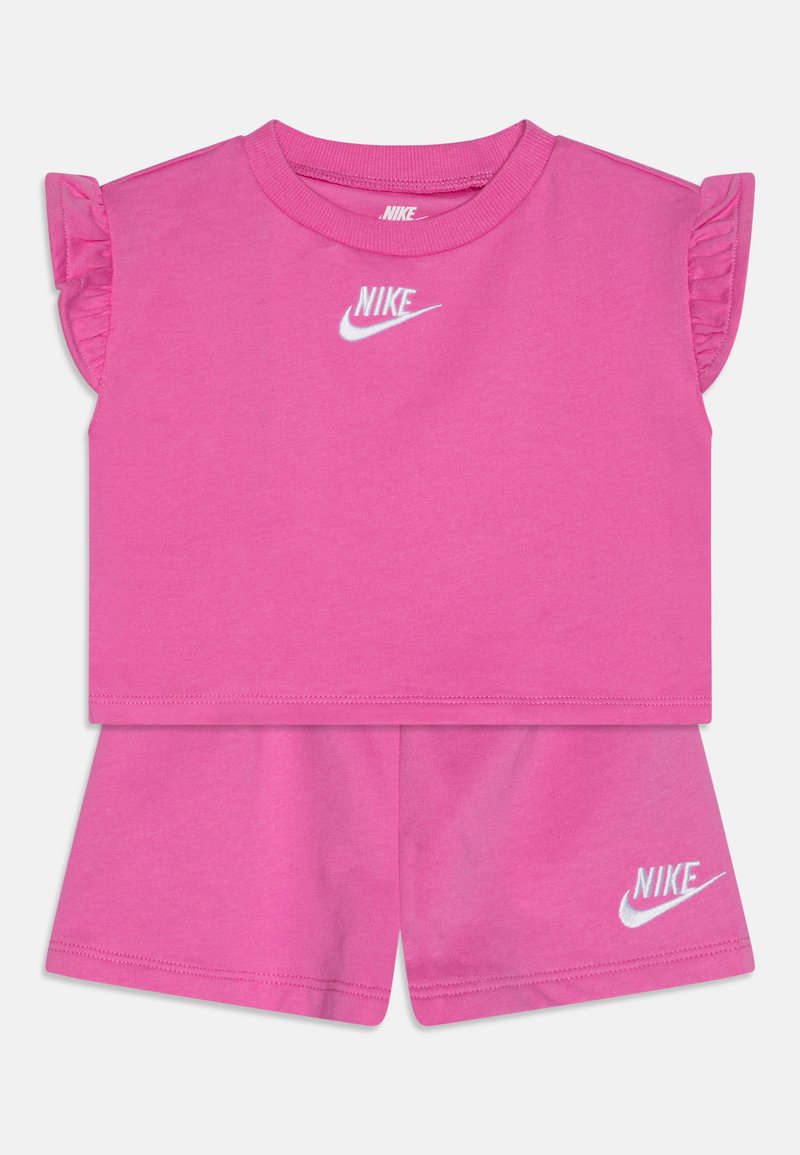 Rožinis medvilninis dušo komplektas, kuriame yra trumpomis rankovėmis palaidinė su volanėlėmis ir derančios šortai, abu su baltu Nike logotipu.