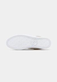 Sohlen aus weißem Gummi mit einem strukturierten Grip-Muster, ausgestattet mit einem runden Logo. Der obere Teil ist in einem hellbraunen Farbton mit einer glatten Oberfläche.