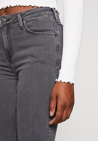 Vaqueros grises de corte slim, con cinco bolsillos, un ligero desgastado y costuras en contraste. Combinados con una camiseta blanca de manga larga con canalé.