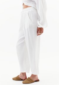Losse witte broek van lichtgewicht stof, met een elastische tailleband, zijzakken en een rechte pijp, in combinatie met geweven instapschoenen.