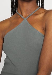 Szary prążkowany top na ramiączkach z dekoltem halter i krzyżowym tyłem, charakteryzujący się gładką fakturą i dopasowanym kształtem.