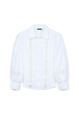 Camicia bianca con colletto a punta, caratterizzata da dettagli in pizzo lungo la parte anteriore e le maniche, e maniche a sbuffo voluminoso.