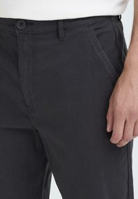 Dark gray cotton trousers featuring a flat front, side pockets, and a single button closure, with a smooth texture and subtle stitching details.
