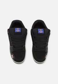 Sapatilhas desportivas pretas com parte superior em malha e camurça, apresentando um logo azul, atacadores pretos, detalhe em vermelho "94" e sola de borracha cinza.