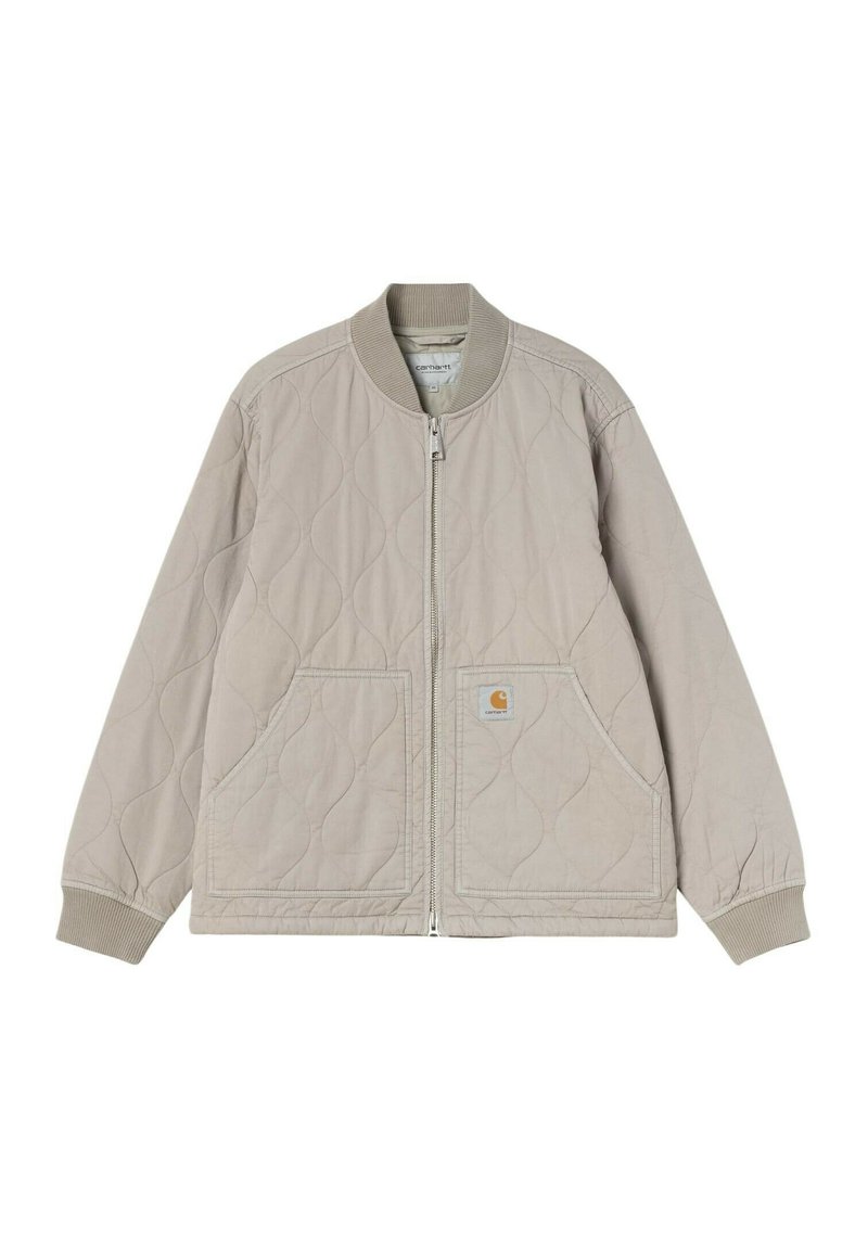 Veste matelassée beige clair avec fermeture éclair frontale, deux grandes poches, col et poignets côtelés, et écusson logo Carhartt sur la poche.
