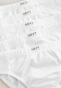 Des slips en coton blanc empilés en rang, présentant des ceintures élastiques avec la marque "NEXT" en noir sur chaque vêtement. Texture lisse et unie.