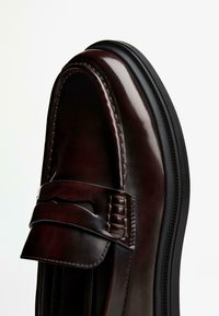 Dark brown leather loafer featuring a rounded toe, decorative strap, contrast stitching, and a black rubber sole.