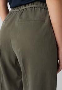 Olive green pants made of lightweight fabric. Features elastic waistband, two back pockets with subtle stitching, and smooth texture.