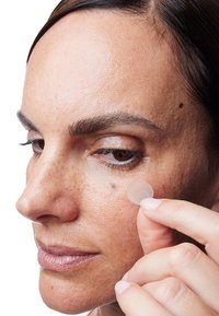 Ein klarer Silikon-Patch wird unter dem Auge auf strukturierte Haut aufgetragen. Natürliches Licht hebt die Hauttöne und feinen Details hervor.