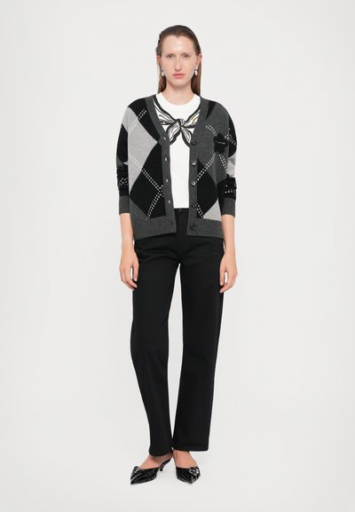 Grå og svart argyle cardigan med knapper, brukt over en hvit topp med sløyfedetalj, sammen med svarte bukser og spisse kanvas sko.