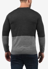 Gray and dark gray long-sleeve sweater with ribbed cuffs and hem, featuring a color-block design. Soft knit texture, fitted shape.
