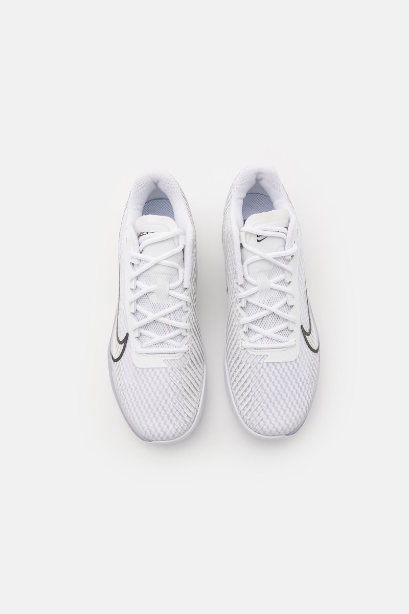 Par de zapatillas deportivas blancas con logotipo negro, textura de malla y cordones blancos vistas desde arriba sobre un fondo blanco liso.