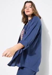 Camicia button-up blu navy realizzata in tessuto testurizzato, con maniche lunghe arrotolate ai polsini e una vestibilità rilassata, leggermente oversize.