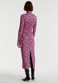 Langes pinkes Blumen Kleid mit langen Ärmeln, hohem Kragen und einem Schlitz auf der Rückseite. Das Material wirkt glatt mit einem dichten, lebendigen Blumenmuster.