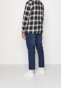Schwarz-weiß karierte Langarmbluse, getragen mit blauen Jeans und weißen Sneakers, die über Knopfdetails und aufgeschlagene Bündchen verfügt.