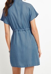 Džínové šaty košilového střihu s krátkými rukávy, zúžené v pase a s rovnou linií, v světle modré barvě a s jemnou texturou.