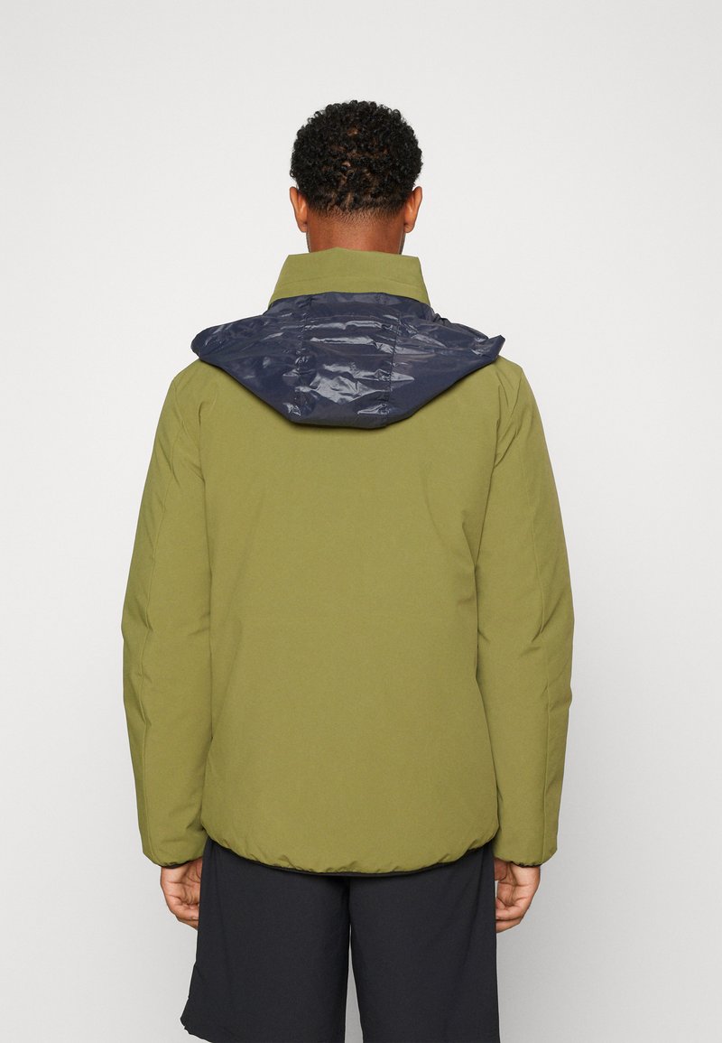 Chaqueta verde oliva con capucha navy brillante, que presenta una textura suave, puños elásticos y un ajuste relajado. Diseño minimalista sin herrajes visibles.