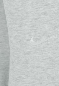 Sudadera gris claro con una tela suave y texturizada. Presenta un pequeño logo de Nike bordado en blanco en la parte frontal. Diseño simple y minimalista.