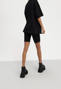 Person wearing black oversized t-shirt, black biker shorts, and black platform lace-up ankle boots standing on light floor.