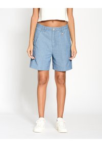Světle modré džíny šortky s hladkým povrchem, předními kapsami, jedním knoflíkem na zapínání a volným střihem, doplněné o bílé tenisky.