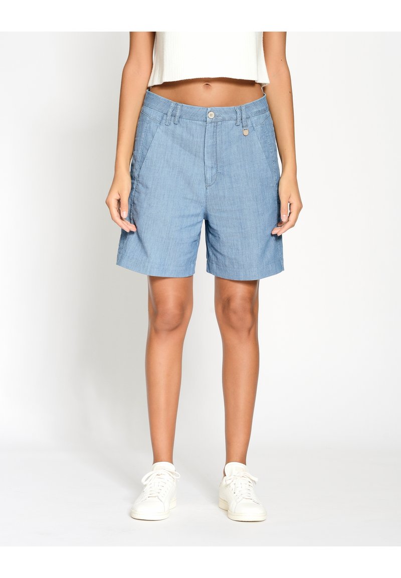 Světle modré džíny šortky s hladkým povrchem, předními kapsami, jedním knoflíkem na zapínání a volným střihem, doplněné o bílé tenisky.