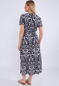 Black and white patterned maxi dress with short sleeves, a fitted waist, and a flowing silhouette. Flat sandals complete the look.