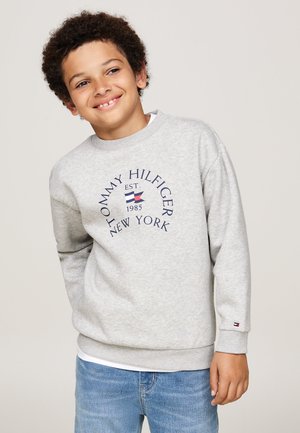 Sudadera gris de tela suave, que presenta un logo redondo con "TOMMY HILFIGER NEW YORK" y un diseño de bandera. Puños y dobladillo acanalados.