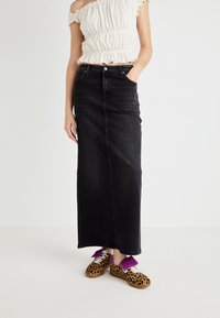 Black denim maxi skirt with a straight cut, featuring front pockets. Paired with leopard print sneakers and purple accents on laces.