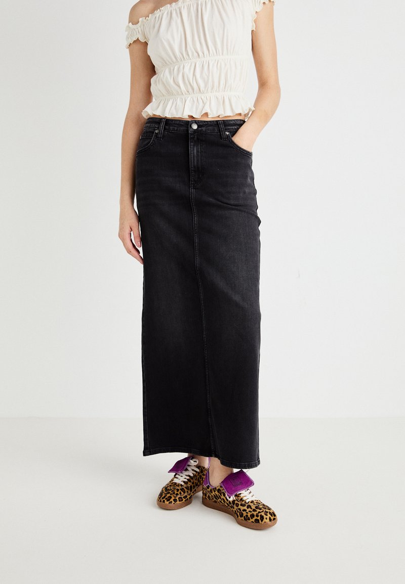 Black denim maxi skirt with a straight cut, featuring front pockets. Paired with leopard print sneakers and purple accents on laces.