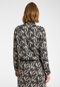 Blůza s barevným vzorem v černobílé kombinaci, s límečkem, dlouhými rukávy a texturovanou tkaninou, která obsahuje abstraktní designy štětcových tahů.