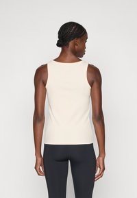 Beige, ribbed, hihaton toppi, jossa on pyöreä pääntie, hieman joustava ja tiukka muotoilu, yhdistettynä mustiin legginsseihin.