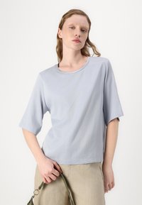 Lyseblå kortermet skjorte med rund hals. Stoffet ser glatt ut og har en litt løs passform. Ingen synlige mønstre eller detaljer.