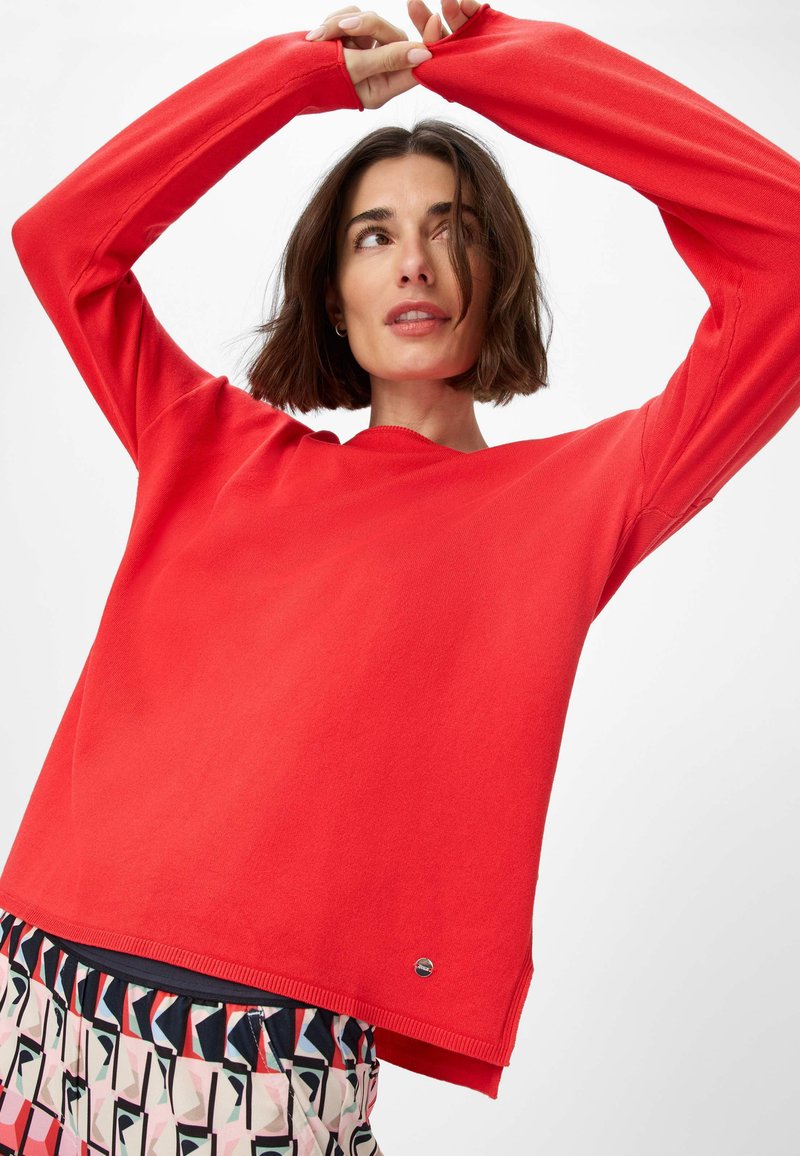 Maglione rosso a maniche lunghe in morbido tessuto, con scollo rotondo e vestibilità comoda. Dettaglio del logo evidente sull'orlo.