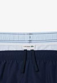 Lacoste zwembroek in lichtblauw en marineblauw. Voorzien van een elastische tailleband met koord, een mesh binnenvoering en een merklabel.