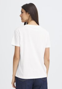 Feh�ér pamut póló rövid ujjakkal, kerek nyakkal és laza szabással, sima felszíne van, minta vagy grafika nélkül.